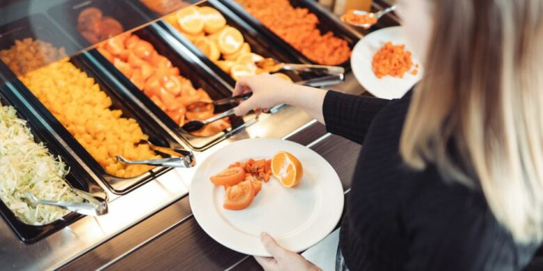 Henkilö ottaa salaattia lautaselle ruokalinjastosta.