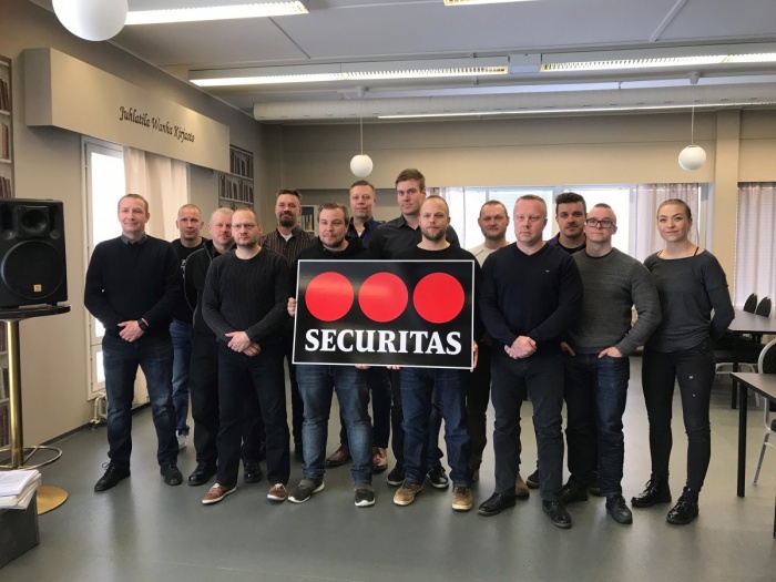 Joukko miehiä seisoo huoneessa Securitas-kyltin kanssa.