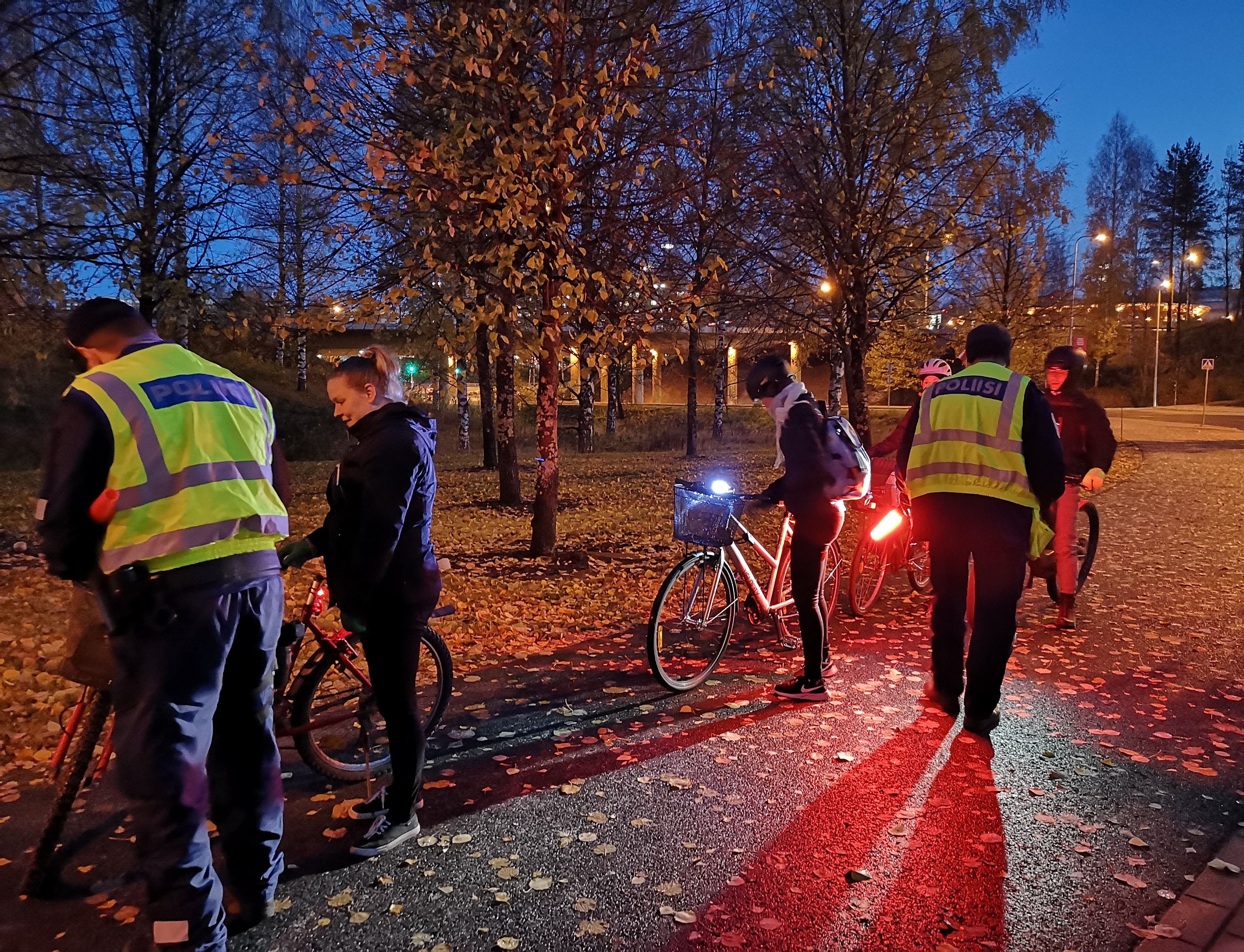 Pimenevässä illassa poliisit jakavat pyöräilijöille heijastimia puiston laidalla.