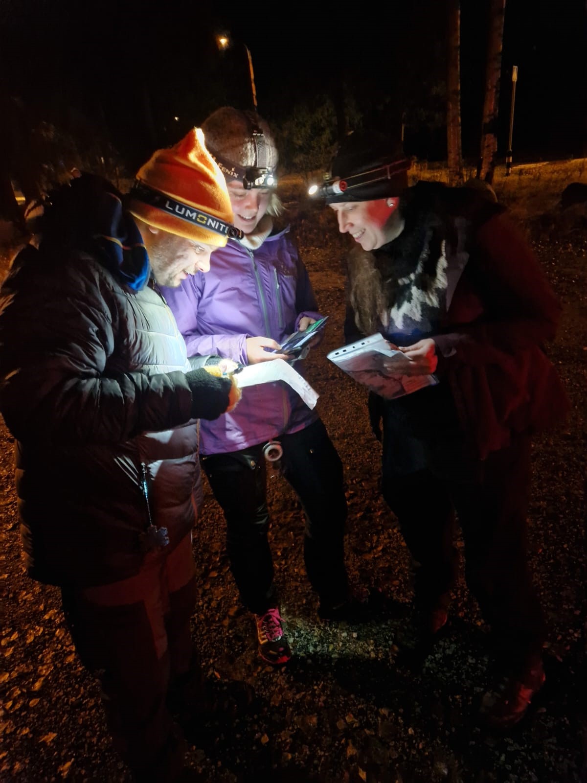 Kolme opiskelijaa lukee pimeässä otsalampun valossa karttaa.