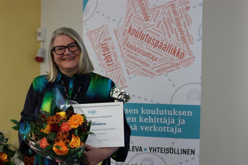 Vuoden opettaja Tiina Meriläinen. Keski-ikäinen harmaatukkainen nainen kukkakimppu kädessä.