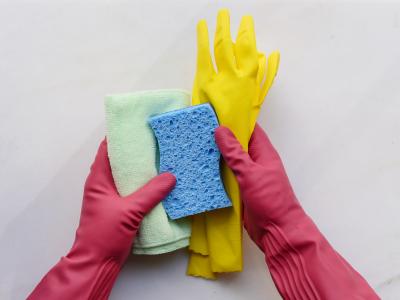 Kädet kumihansikkaissa pitelevät siivoustuotteita.