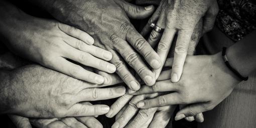 Mustavalkoinen kuva, jossa on eri ikäisten ihmisten käsiä yhdessä.
