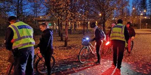 Pimenevässä illassa poliisit jakavat pyöräilijöille heijastimia puiston laidalla.