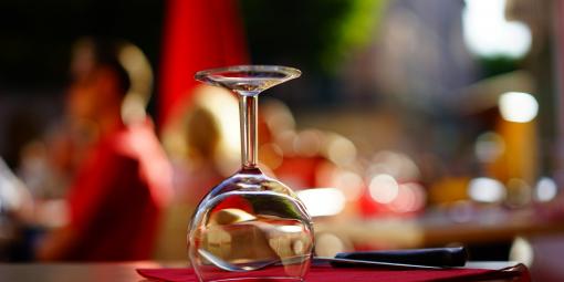 Ravintolan pöydällä on punainen servetti, jonka päällä on viinilasi alassuin ja aterimet.