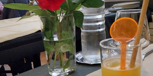 Pöydällä taustalla maljakossa punainen kukka ja etualalla keltaista juomaa drinkkilasissa.