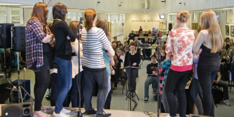 Kymmeniä opiskelijoita koulun salissa kuuntelemassa puhetta.