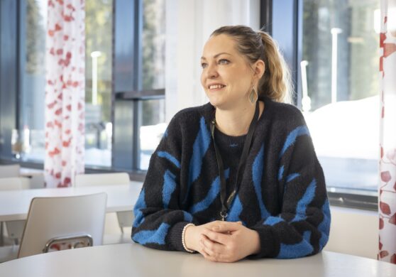 Ihminen istuu pöydän ääressä ja hymyilee.