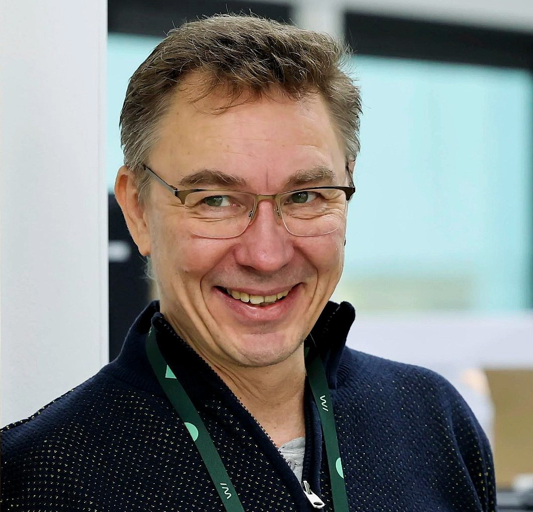 Ylävartalokuva jossa keski-ikäinen lyhythiuksinen mies katsoo hieman ohi kameran ja hymyilee.