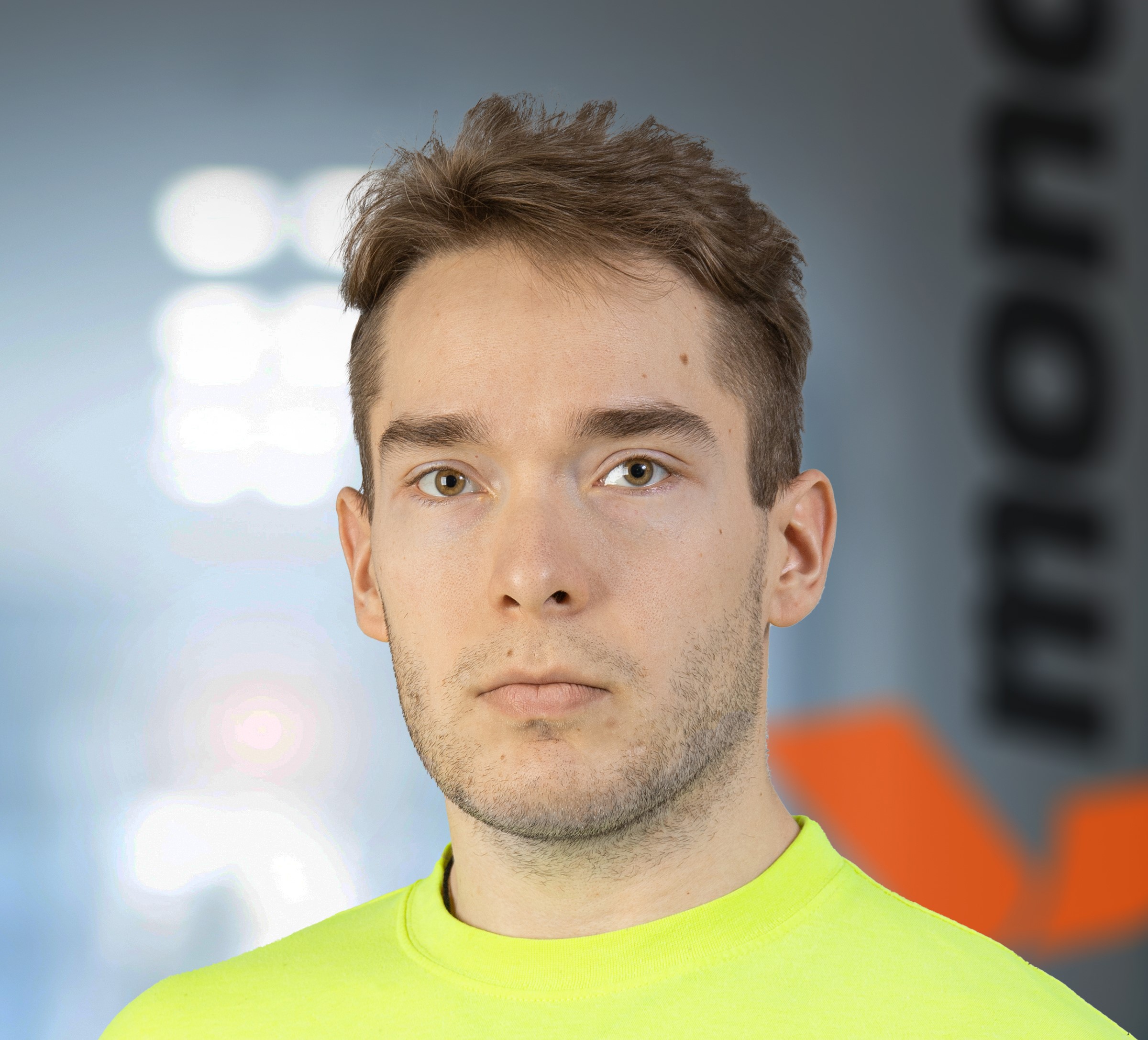 Nuori ruskeahiuksinen mies jolla on keltainen Mondi-logollinen paita päällä ja katsoo kameraan.