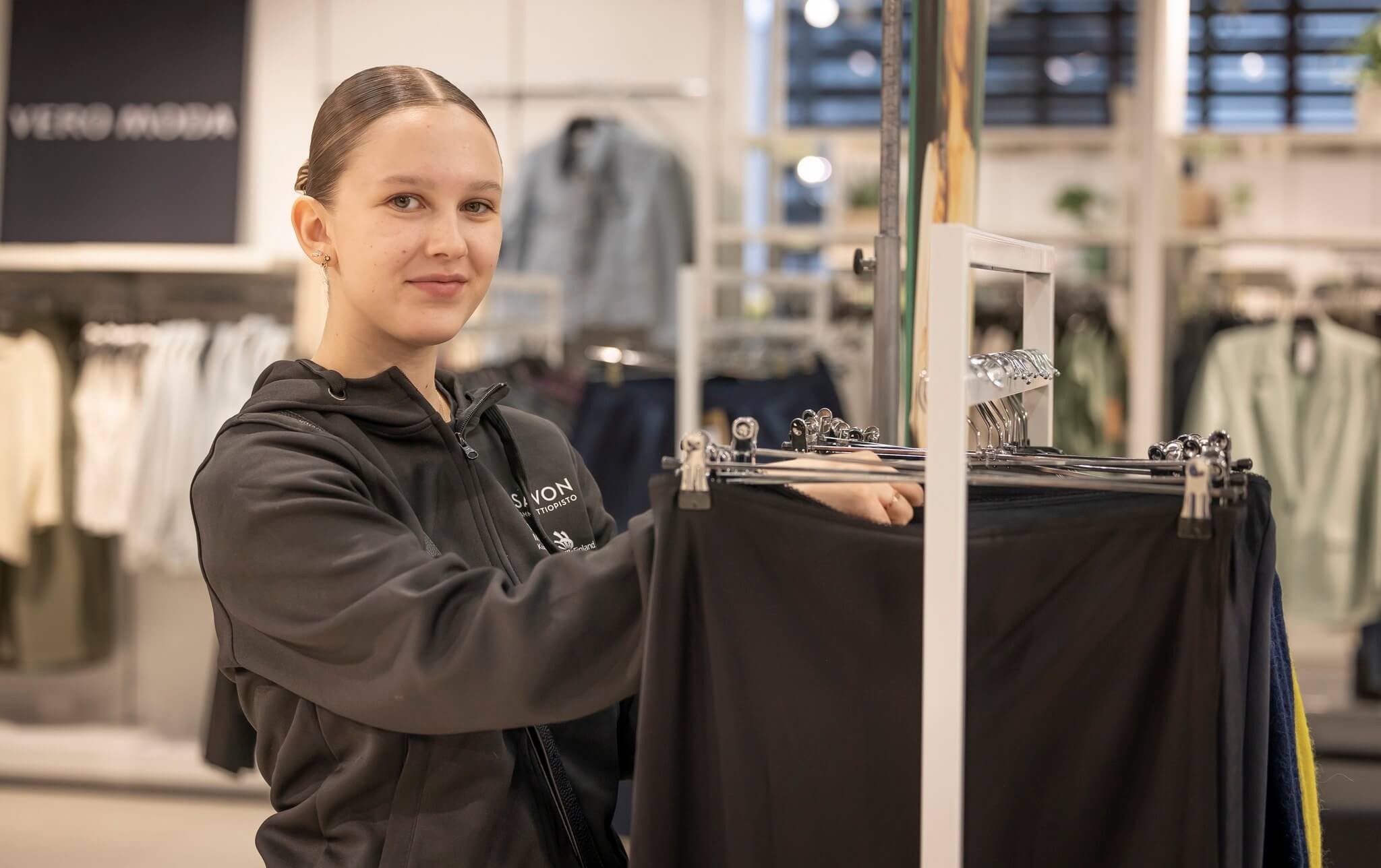 Opiskelija laittaa housuja henkareihin myytäväksi.