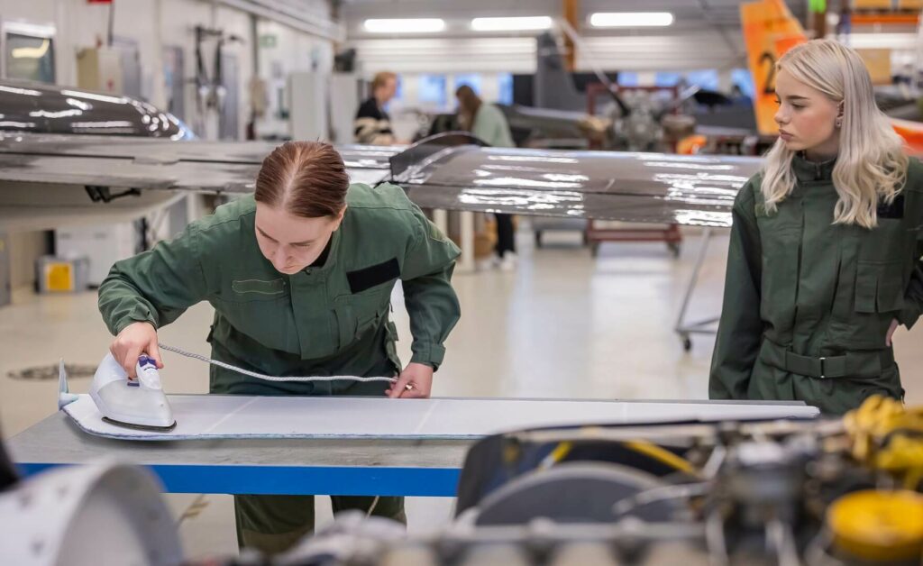 Opiskelija silittää verhoilukangasta. Toinen opiskelija seuraa vierestä.