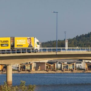 Yhdistelmäajoneuvo ajaa siltaa pitkin. Taivas ja vesi ovat sinisiä.