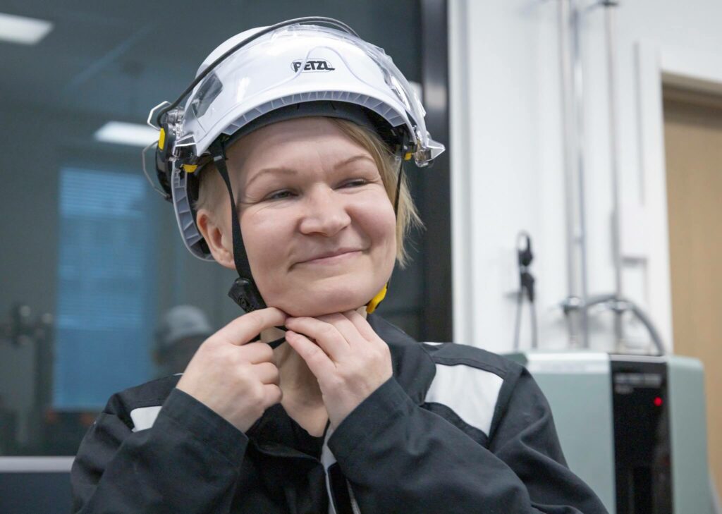 Iloinen henkilö laittaa valkoisen kypärän päähänsä.
