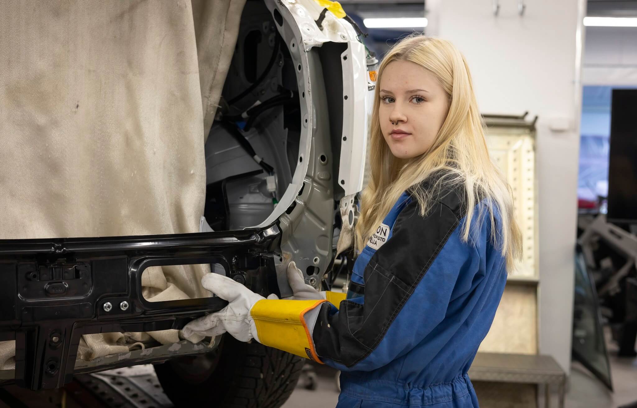 vaaleahiuksinen nainen laittaa auton peltiä paikalleen