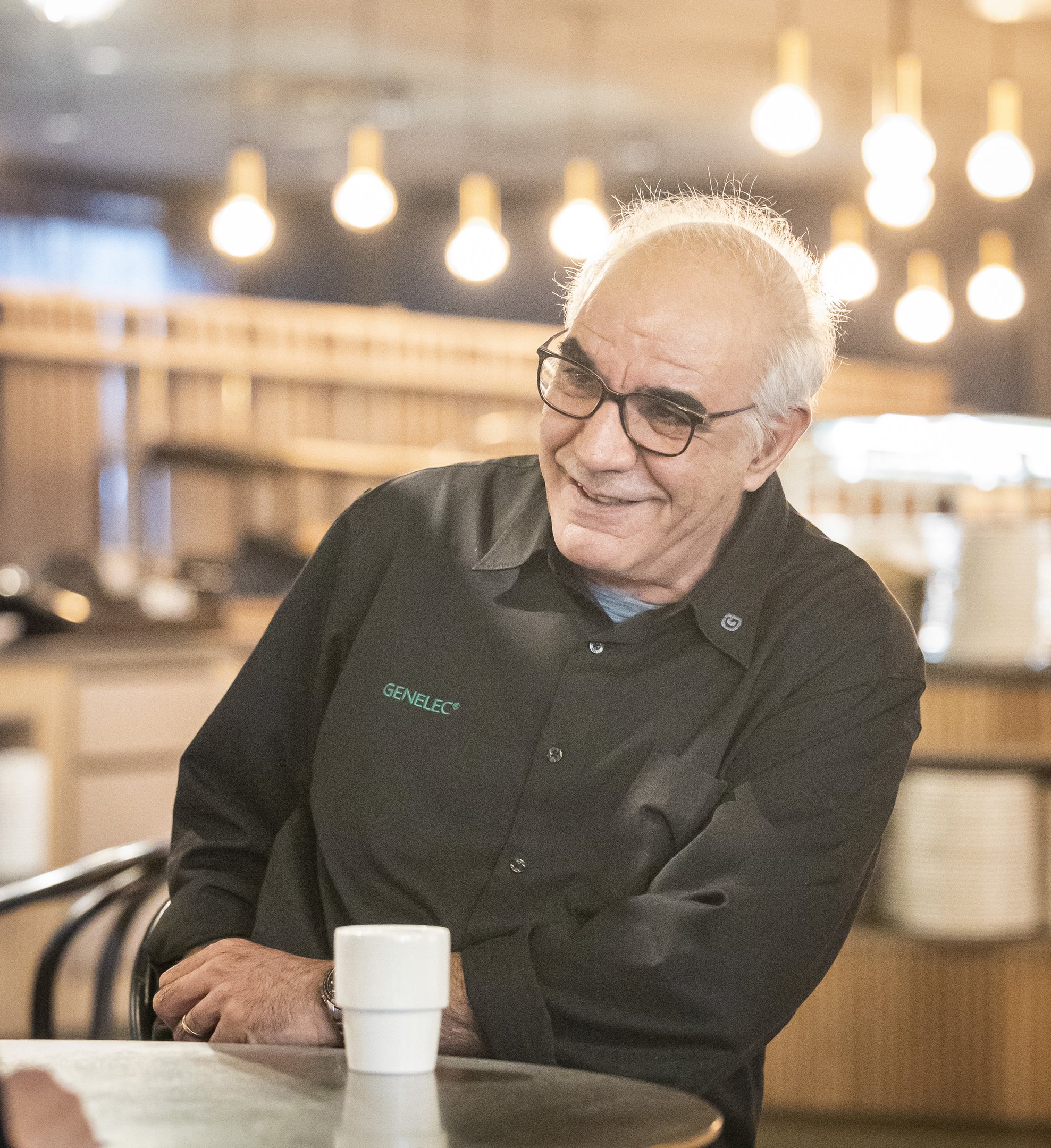 Siamäk Naghian istuu pöydän ääressä hymyillen ja kahvikuppi on pöydällä.