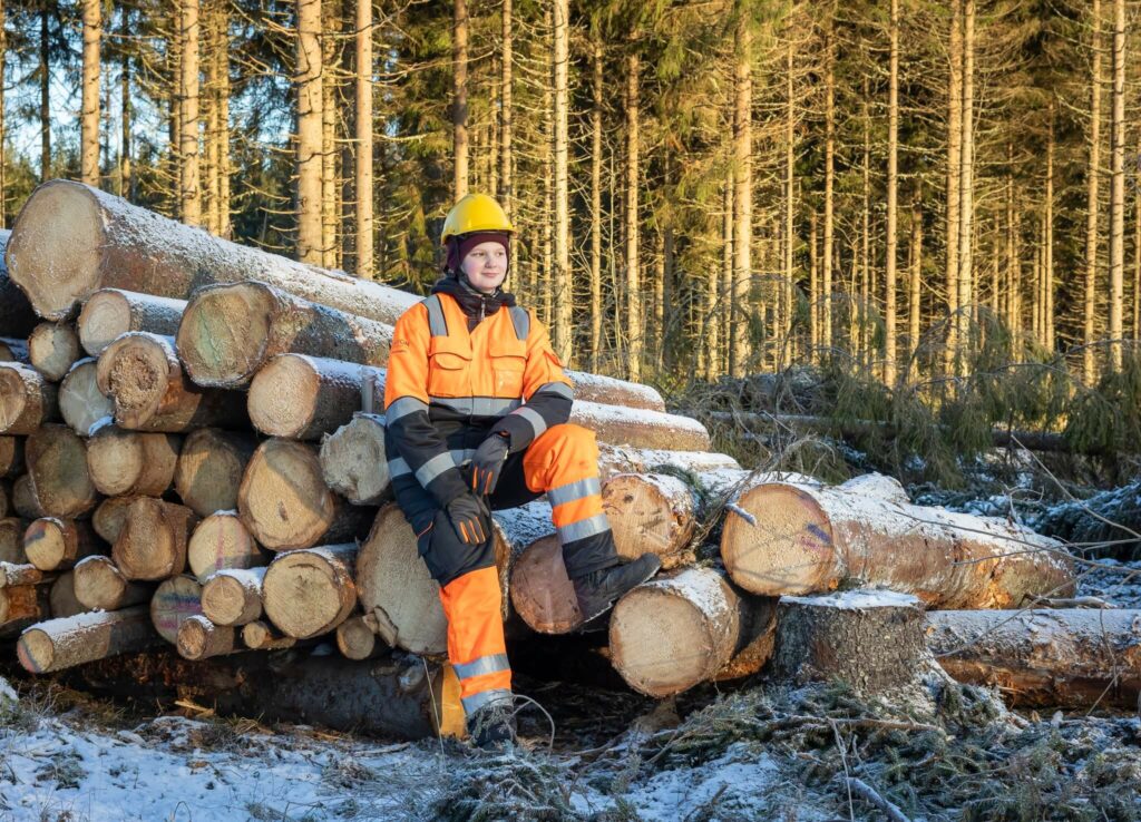 Opiskelija istuu tukkipinon päällä.