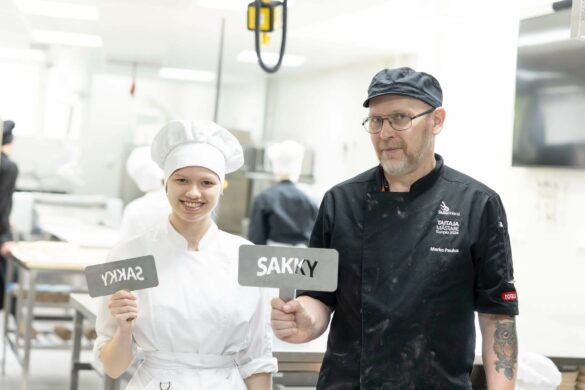 opettaja ja opiskelija seisovat leipomossa kyltit kädessään. Kyltissä lukee sakky.