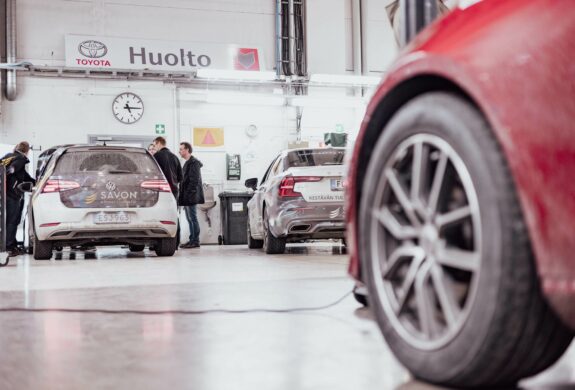 autohalli, jossa ihmisiä seisoo auton vieressä.