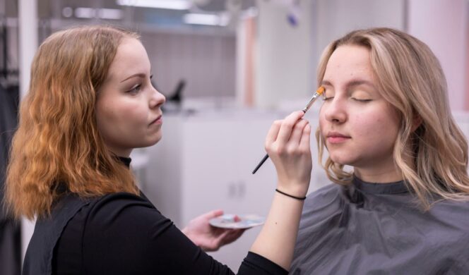 Opiskelija laittaa asiakkaan luomiin luomiväriä siveltimellä.