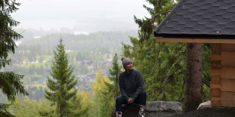 Henkilö istuu metsämaisemassa kodan edessä.