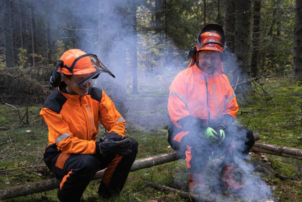 Kaksi miestä nuotion ääressä metsässä.
