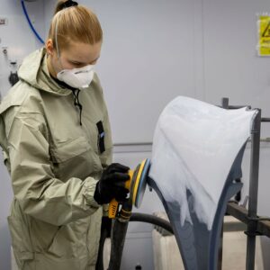 haalariasuinen nainen hioo autonpeltiä