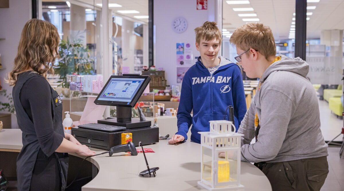 Kaksi opiskelijaa on asiakkaana Sakky Shopissa ja kolmas opiskelija on tiskin takana palvelemassa.