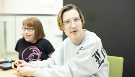 Kaksi opiskelijaa istuu vierekkäin sohvalla ja toinen katsoo kameraan.