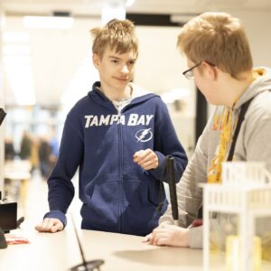 Kaksi opiskelijaa nojaa Sakky Shopin tiskiin ja katsoo toisiansa.