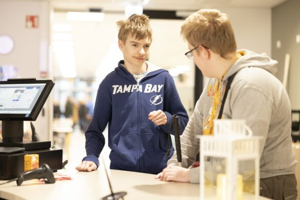 Kaksi opiskelijaa nojaa Sakky Shopin tiskiin ja katsoo toisiansa.