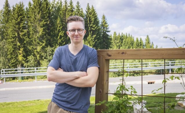 Nuorehko henkilö nojaa puukaiteeseen ulkona kesäisenä päivänä.