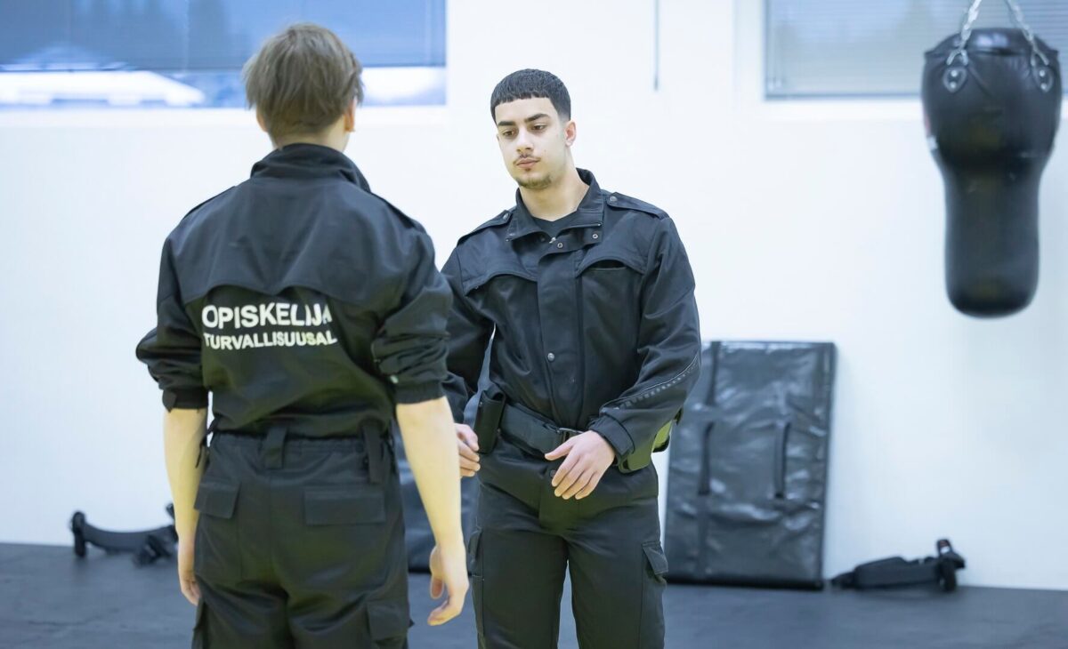 Kaksi opiskelijaa työhaalareissa harjoittelemassa voimankäyttöä.