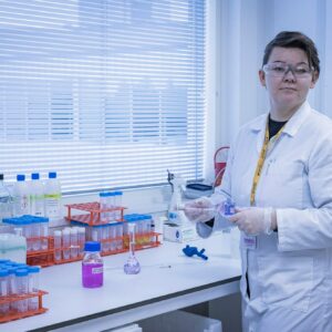 nainen seisoo pöydän ääressä ja kädessä on laboratorioalan työvälineitä.