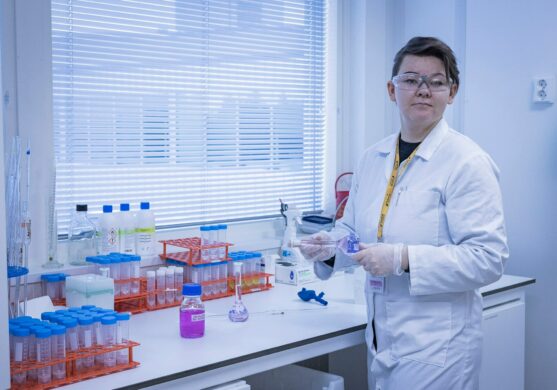 nainen seisoo pöydän ääressä ja kädessä on laboratorioalan työvälineitä.