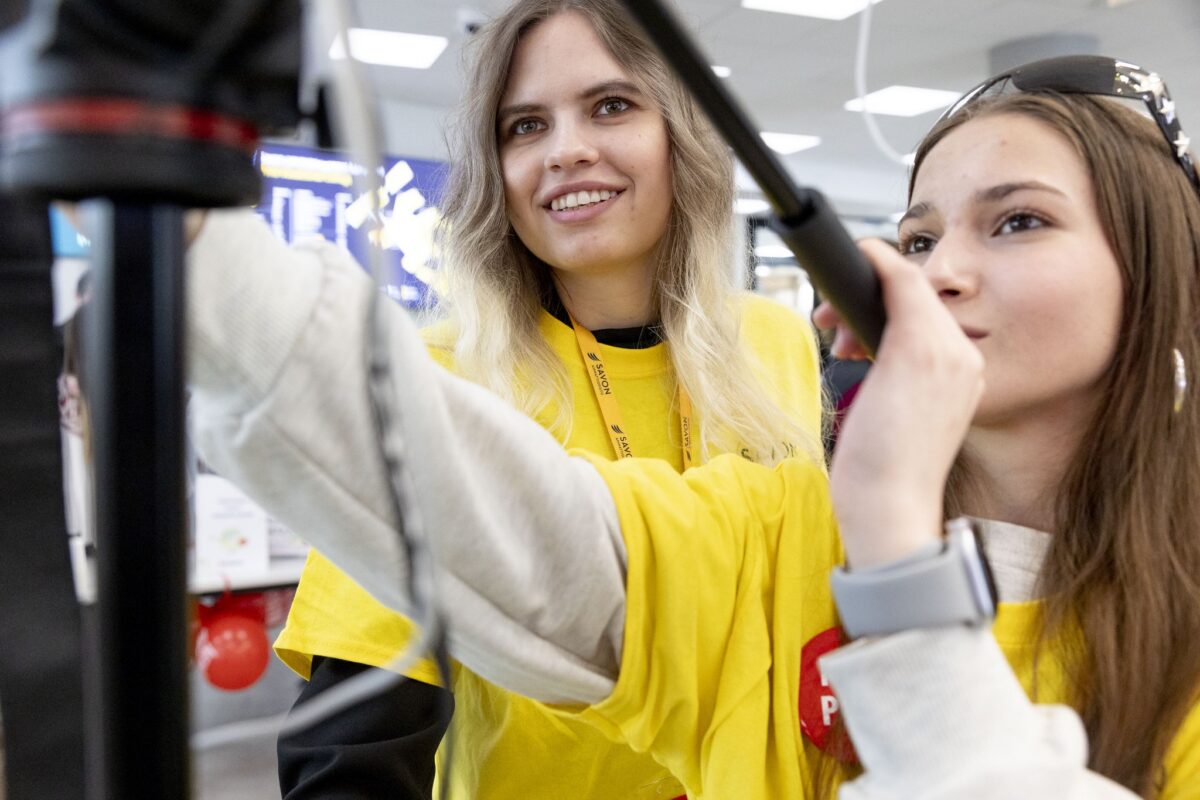 Keltapaitaiset opiskelijat katsovat kameran ruutua.