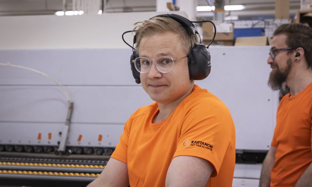 Ihminen, jolla on oranssipaita ja kuulosuojaimet, katsoo kameraan.