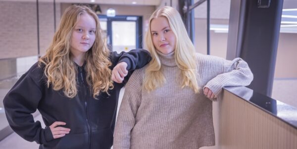 Kaksi opiskelijaa seisoo ja katsoo kameraan. Toisen käsi nojaa toisen olkapäähän ja toisen käsi kaiteeseen.