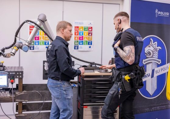 kaksi henkilöä seisoo hitsausrobotin edessä.