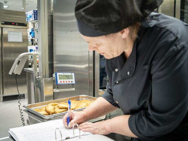 Kokki tekee raporttia raporotintikansioon. Taustalla rosterisia keittiökoneita.