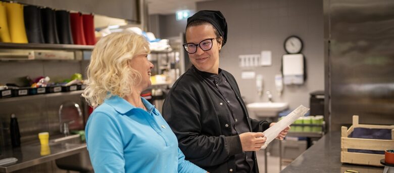 Kaksi henkilöä katsovat toisiaan hymyillen keittiössä